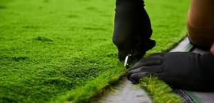 Man with black gloves cutting artificial grass